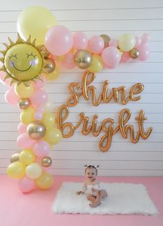 a baby is sitting in front of some balloons with the words shine bright on it