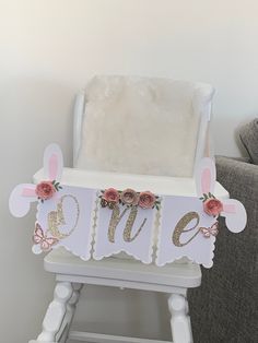 a white chair with pink flowers on it and the word me spelled in gold letters