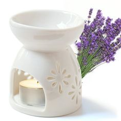 a white candle holder with lavender flowers in it and a lit candle next to it