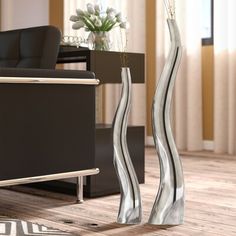 two tall metal vases sitting on top of a wooden floor next to a couch