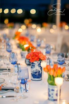 a long table is set with blue and white china vases, orange flowers, and candles