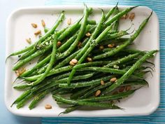 green beans with almonds on a white plate next to a blue striped tablecloth