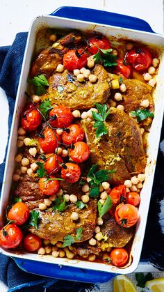 a casserole dish with meat, tomatoes and chickpeas in it on a blue cloth