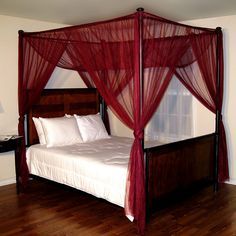 a four poster bed with red netting on the headboard and foot board, in a bedroom