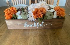 a wooden box filled with white and orange flowers sitting on top of a wooden table