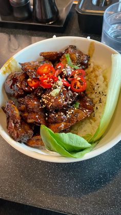 a white bowl filled with meat and rice on top of a counter next to a glass of water