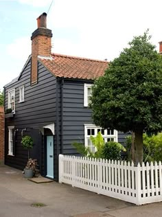 a black house with white picket fence and trees in the front yard on a sunny day