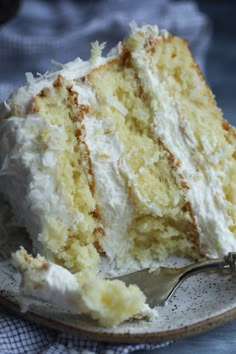 a piece of white cake on a plate with a fork in the foreground and a napkin behind it