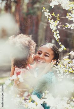 a woman holding a child in her arms and smiling at the camera with white flowers around her