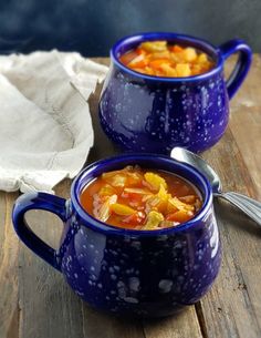 two blue mugs filled with soup on top of a wooden table