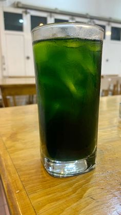 a glass filled with green liquid sitting on top of a wooden table