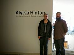 two people standing next to each other in front of a sign