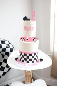 a two tiered cake sitting on top of a white table next to a black and white checkered chair