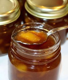 a spoon full of honey sitting on top of a jar filled with liquid next to other jars