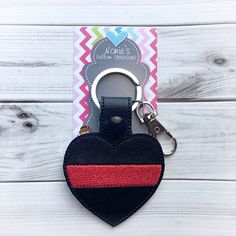 a heart shaped leather keychain with a red and black stripe on the front