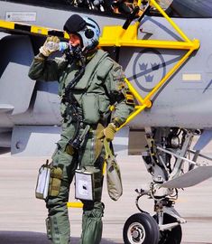 an air force pilot standing in front of a fighter jet drinking from a water bottle