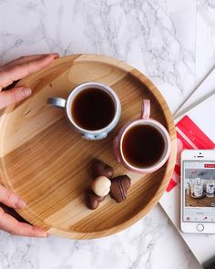 two hands holding cups of coffee on a wooden tray