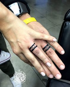 two people holding hands with tattoos on their fingers and one has a yellow ring in the middle