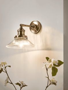 a light that is on the side of a wall with flowers in front of it