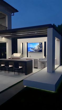 an outdoor kitchen and dining area with a large screen tv on the wall at night