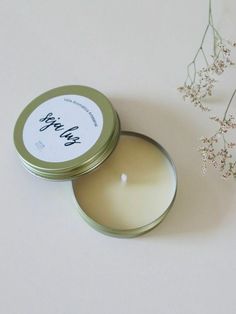 an open tin candle sitting on top of a white table next to a small plant