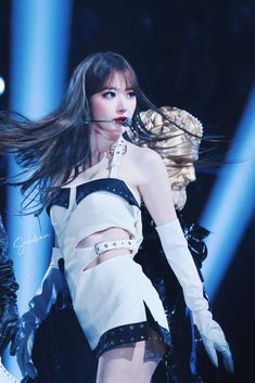 a woman in white and black outfit on stage with her hair blowing in the wind