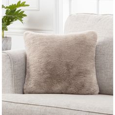 a beige pillow sitting on top of a couch next to a potted green plant