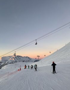 skiers are skiing down a snowy slope at sunset or dawn with ski lift in the background