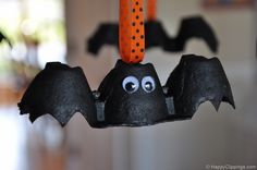 some black bats hanging from a string with orange and black decorations on it's head