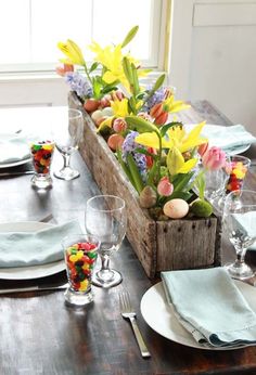 a wooden crate filled with flowers on top of a table next to plates and silverware