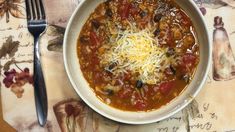 a white bowl filled with chili and cheese on top of a table next to a fork