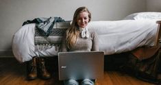 a woman sitting on the floor with her laptop in front of her, looking at the camera