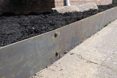 a metal planter filled with dirt next to a brick building