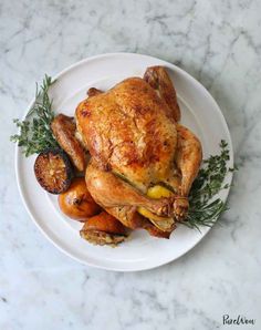 a white plate topped with a roasted chicken and veggies on top of a marble counter