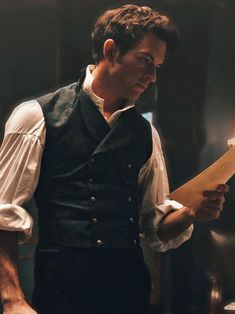 a man in a black vest and white shirt is holding a piece of paper while looking at something