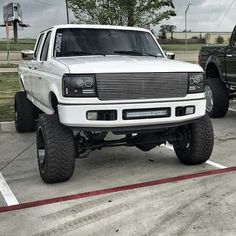 a white truck parked in a parking lot next to another black truck with large tires