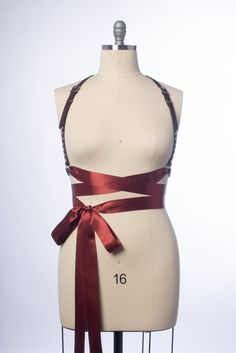 High quality, durable-yet-delicate bespoke harness made in leather or PVC. Embellished with studs along straps. Luxurious wide satin ribbons wrap around the waist and tie into a bow. Silver-toned nickel plated steel hardware. Shown in natural tan leather and oxblood leather. All colors have matching ribbon ties (clear has black ribbon). Also available in PVC and vegan leather. Custom sizing available. All pieces are MADE TO ORDER, standard sizes XS-4XL. If your measurements fall outside these st Harness Design, Fabric Harness, Women Bow Tie Outfit, Ribbon Harness, Fashion Harness, Diy Harness, Goth Harness, Ribbon Outfit, Leather Strapped Harness