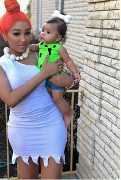 a woman in a white dress holding a baby wearing a green shirt and orange hair