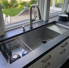 a stainless steel kitchen sink in front of a window with the view of a yard