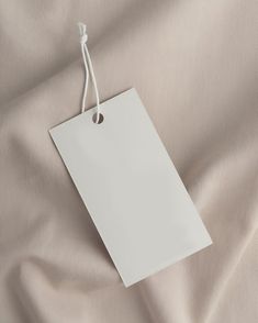 a white paper tag hanging from a string on top of a sheet of beige fabric