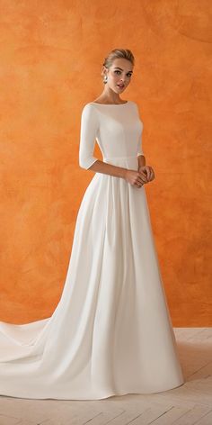 a woman in a white wedding dress standing against an orange wall