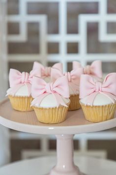 three cupcakes with pink bows are sitting on a cake plate