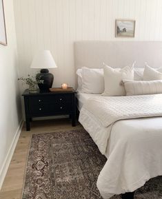 a bed with white linens and pillows in a bedroom next to a rug on the floor