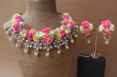 a necklace with flowers and pearls is on display next to a vase filled with other jewelry