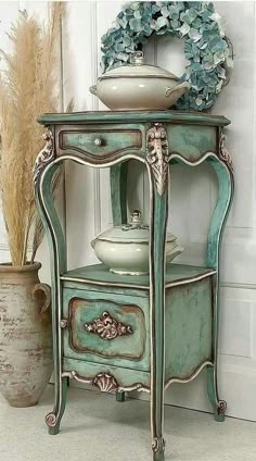 an old blue cabinet with a bowl on top and flowers in the vase next to it