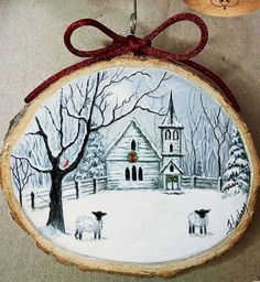 a christmas ornament hanging on a wall next to a wooden slice with a painting of sheep in front of a church