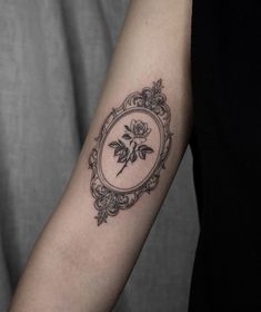 a woman's arm with a rose in a frame tattoo on the left forearm