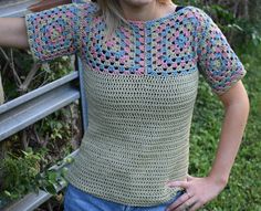 a woman wearing a crochet top standing next to a wooden fence with her hands on her hips