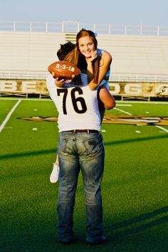 a man holding a woman on his back while standing in front of a football field