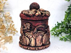 a ceramic container with an image of pumpkins and leaves on the lid next to some flowers